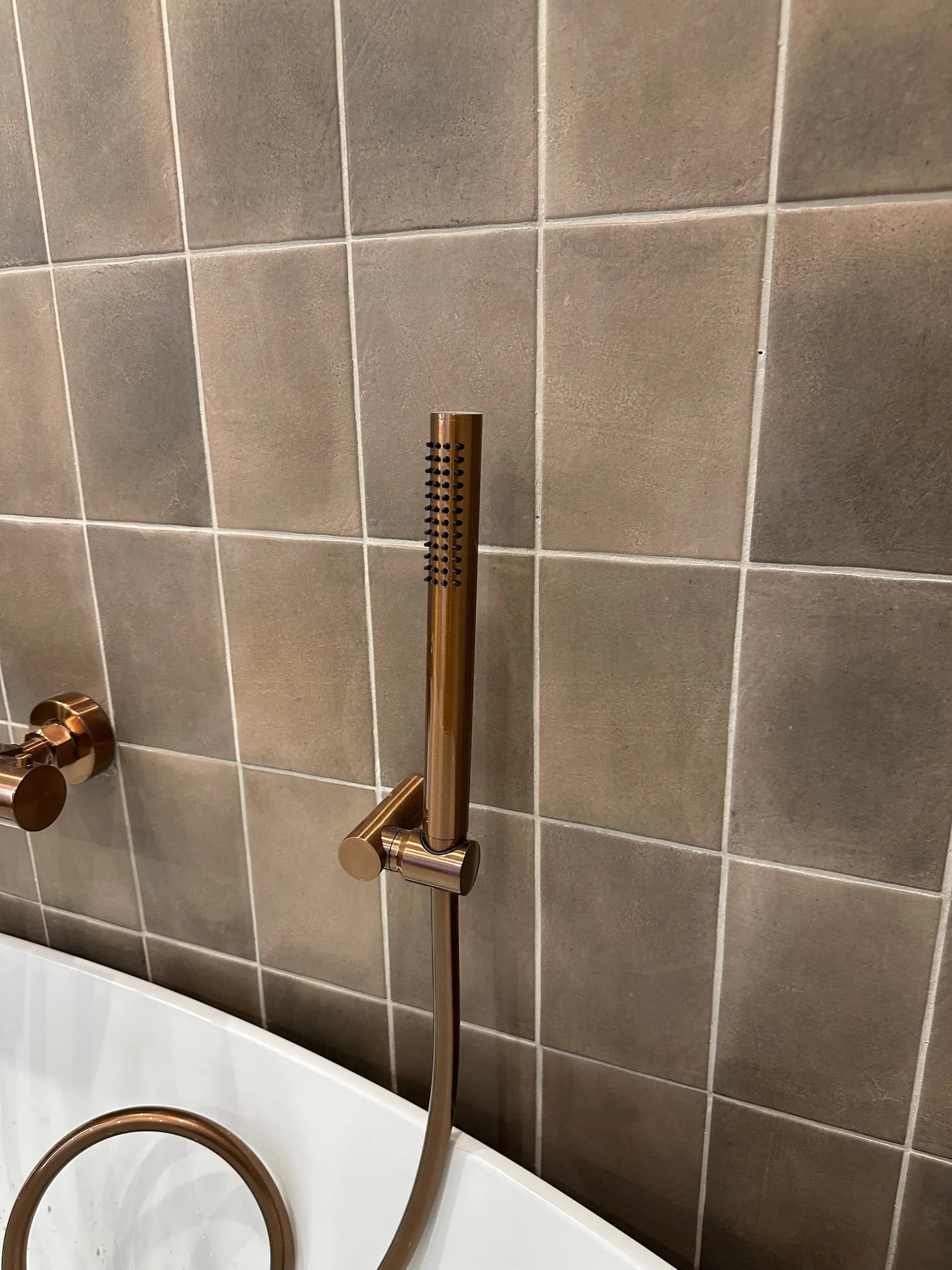 Geborsteld bronzen handdouche bij vrijstaand bad met warme bruine accenttegels