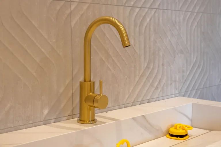 Goudkleurige wastafelkraan met marmerlook wasbak en reliëf wandtegels in de Renova badkamershowroom