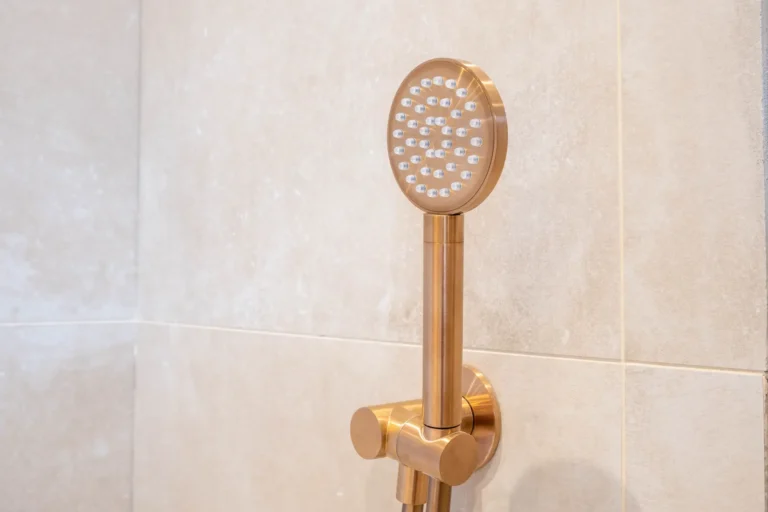 Koperkleurige handdouche tegen beige wandtegels in de Renova badkamershowroom