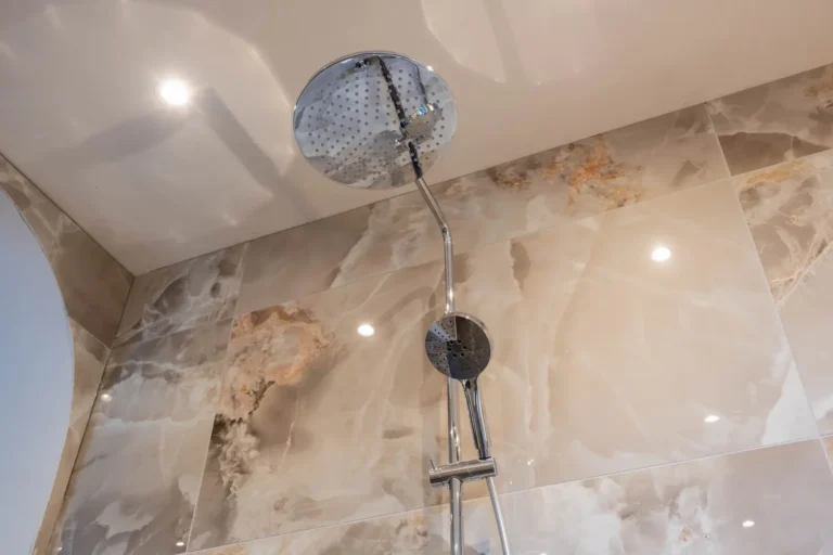 Chromen regendouche met handdouche en beige marmerlook wandtegels in de Renova badkamershowroom