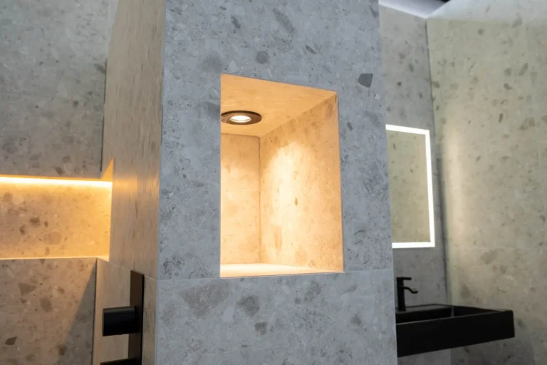 Verlichte wandnissen in een terrazzolook badkamer met ledspiegel en zwart badmeubel in de Renova badkamershowroom