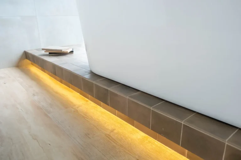 Vrijstaand bad op een betegeld podium met warme ledverlichting in de Renova badkamershowroom