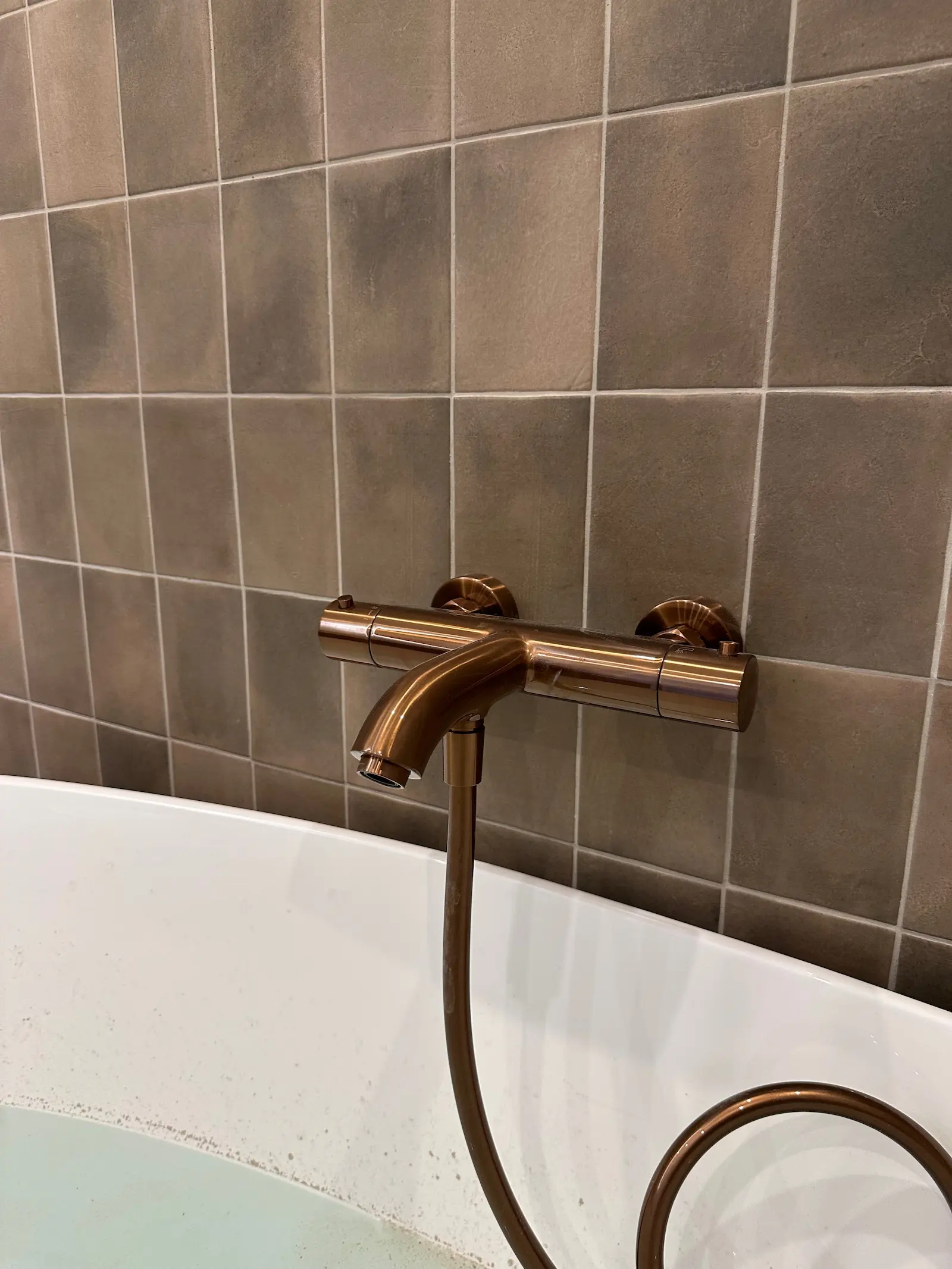 Geborsteld bronzen thermostatische badkraan bij vrijstaand bad met bruine accenttegels