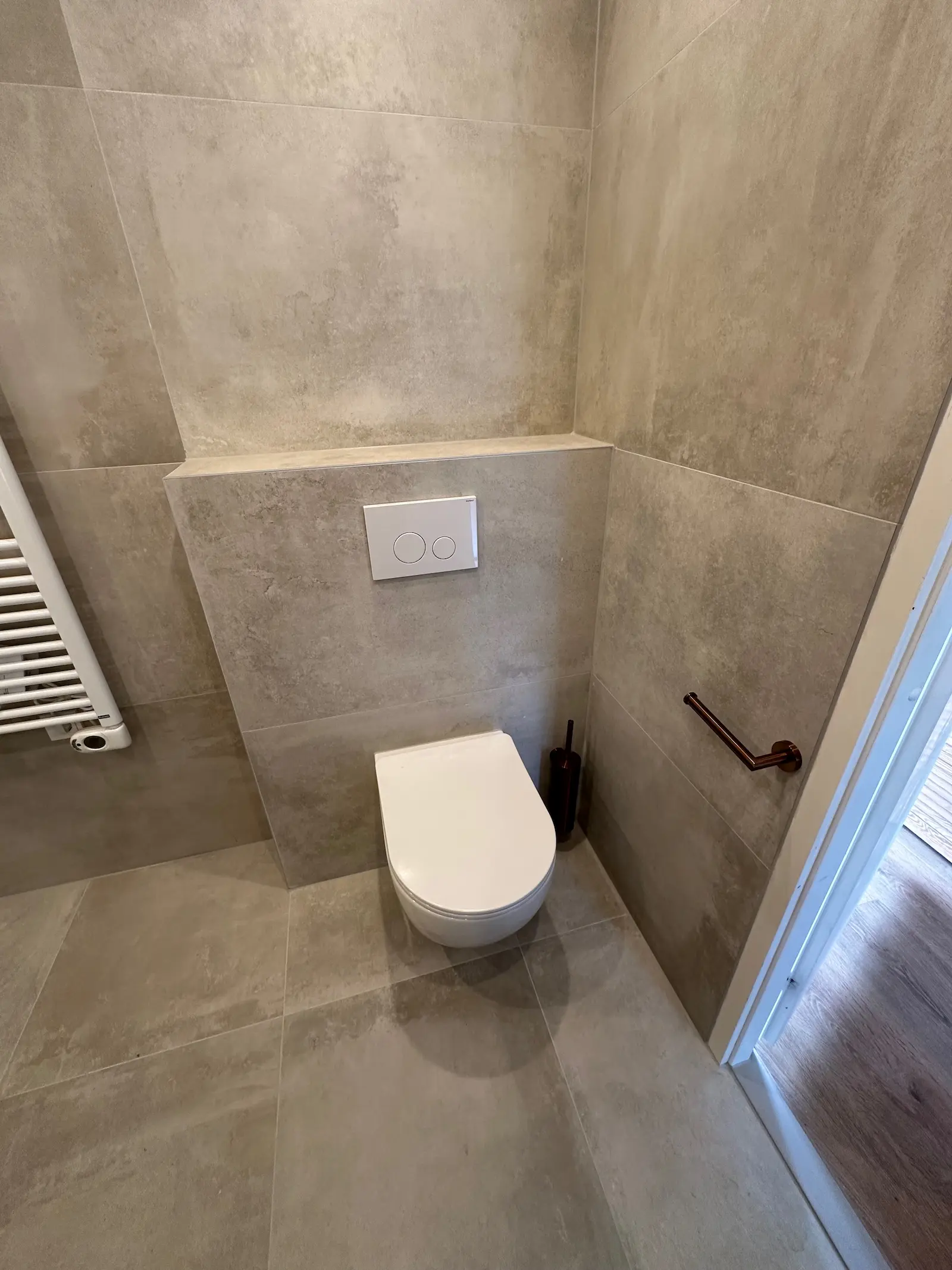 Wandtoilet met betegelde ombouw, witte drukplaat en bronskleurige accessoires