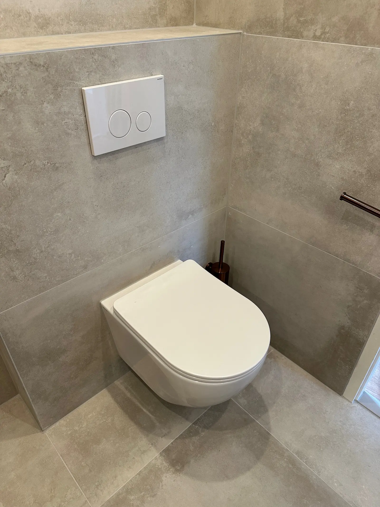 Wit wandtoilet met inbouwreservoir, witte drukplaat en grote grijze badkamertegels