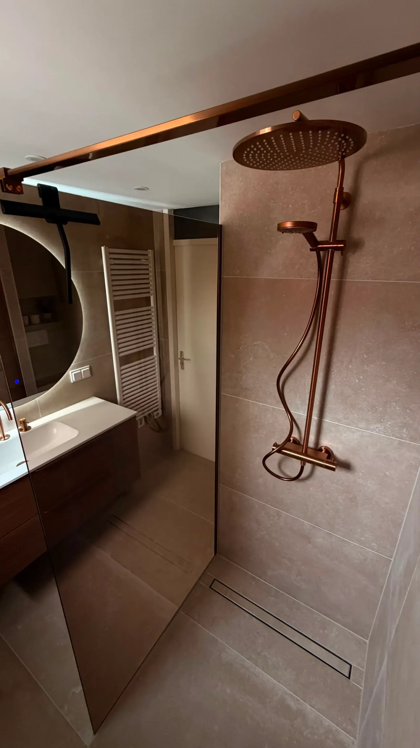 Overzicht van een moderne badkamer met ruime inloopdouche, glazen douchewand en bronskleurige regendouche