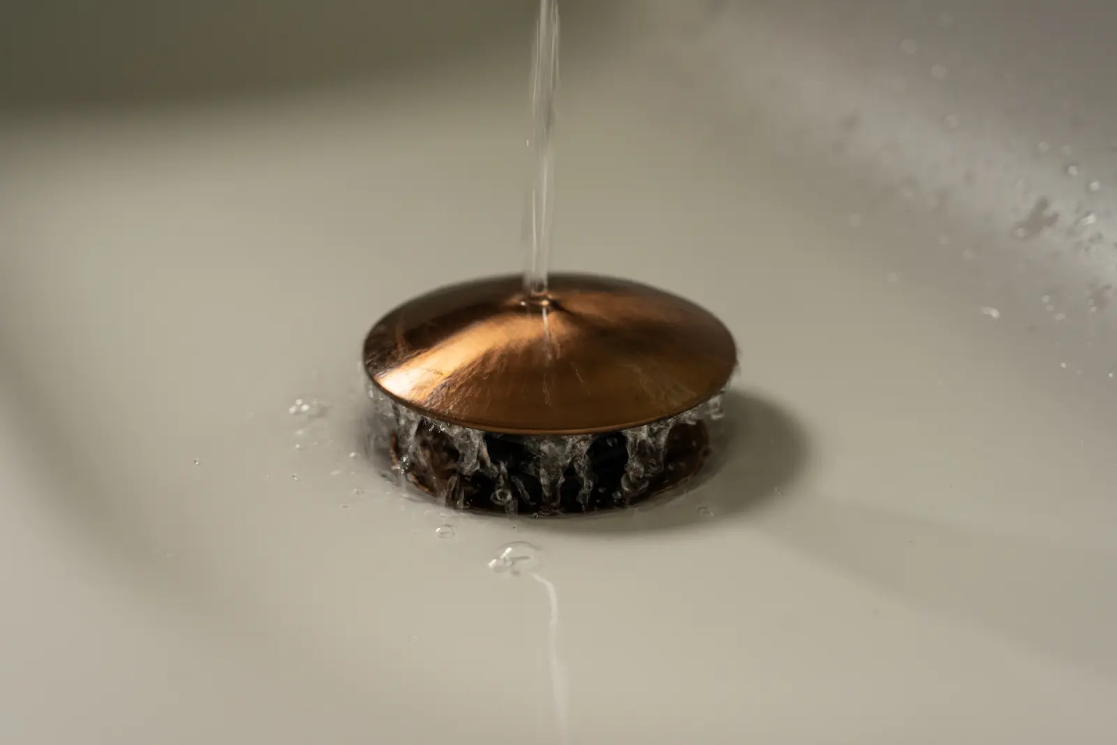 Designplug in geborsteld koper in de witte wastafel van een gerenoveerde badkamer in Spijkenisse