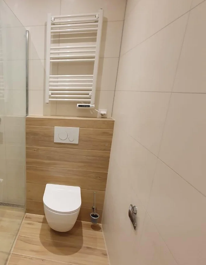 Hangtoilet tegen een houtlook wand met handdoekradiator in een gerenoveerde badkamer