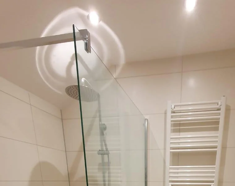 Regendouche en glazen douchewand in een gerenoveerde badkamer met witte wandtegels