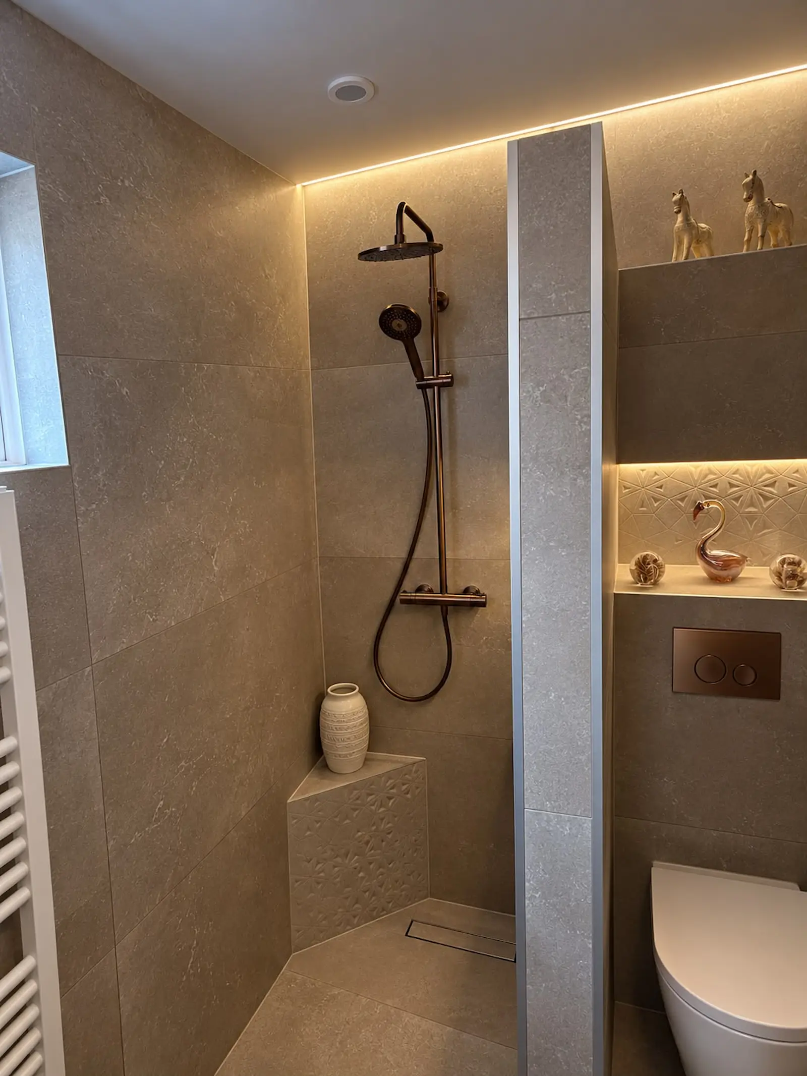 Luxe inloopdouche met bronzen regendouche, verlichte nis en grote beige tegels in Rozenburg