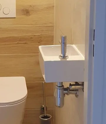 Klein wit fonteintje met chroom kraan en een wandlamp erboven in het gerenoveerde toilet